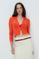 Woman wearing an orange Cecilia cardigan white skirt with belt on a white background, detail front view 